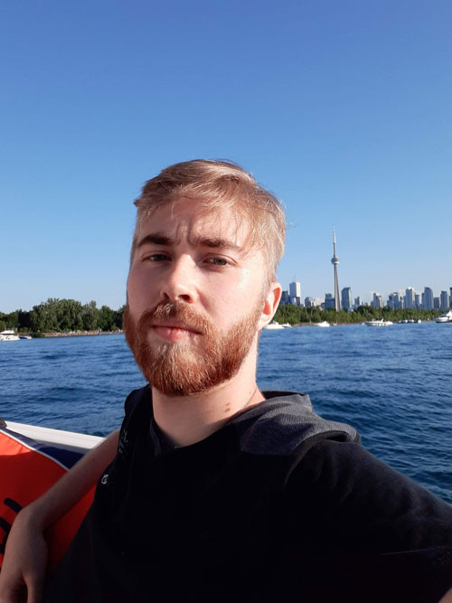 Toronto SEO Expert, Johnny Baskin, sitting in a boat with the Toronto Skyline and CN tower behind him.